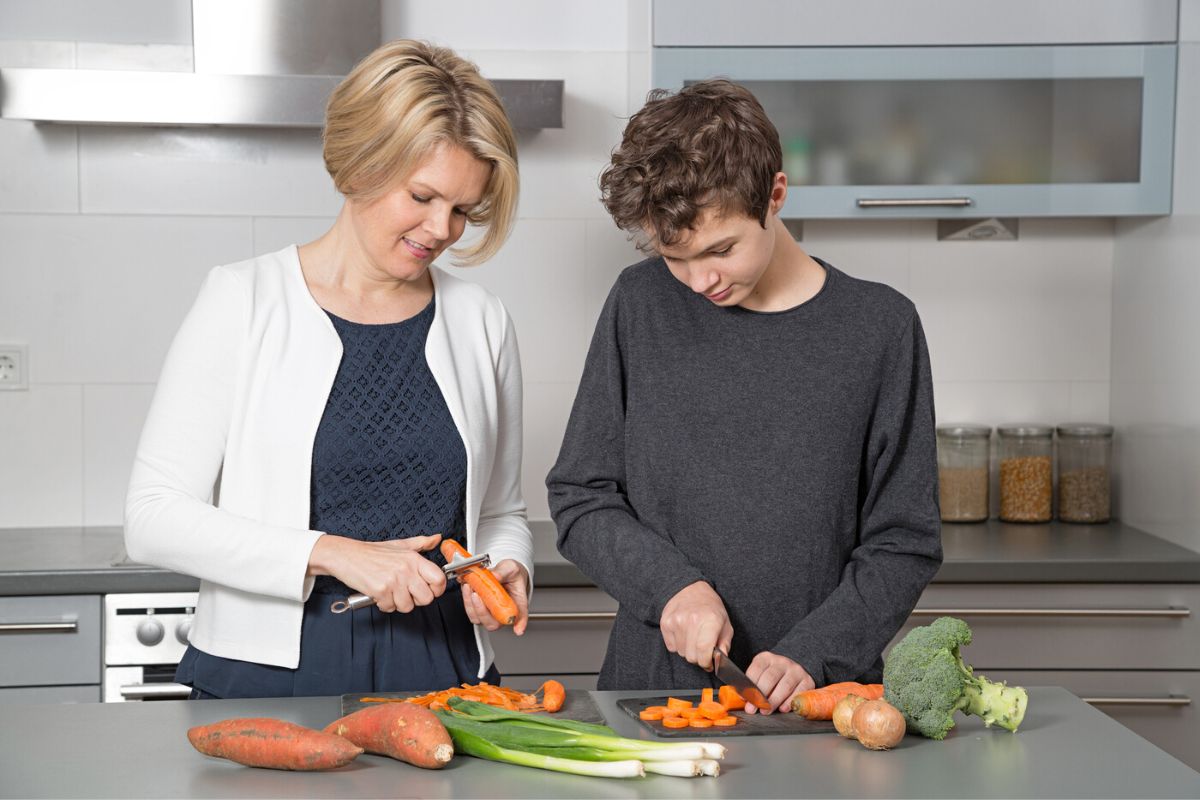 13 year old teen boy chopping vegetables next to mother