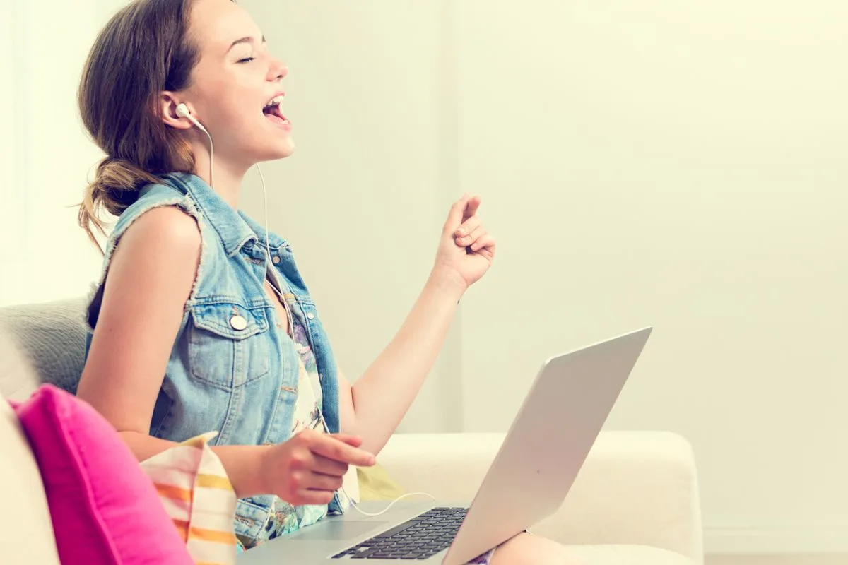 15 year old girl with earbuds and laptop on couch, belting out lyrics over Zoom