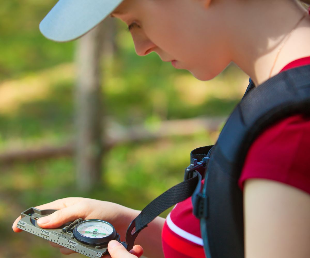 teen girl in red shirt and hat using compass while geocaching