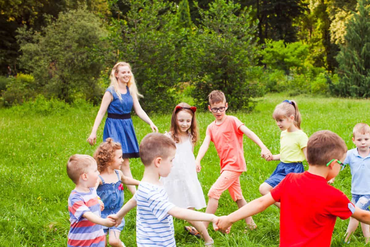 group of kids at park with tween supervising, playing ring around the rosie