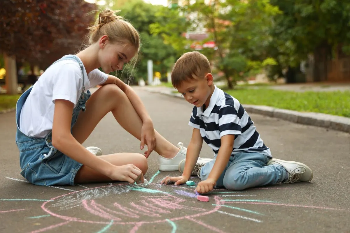 12 year old girl playing with chalk with younger child outside
