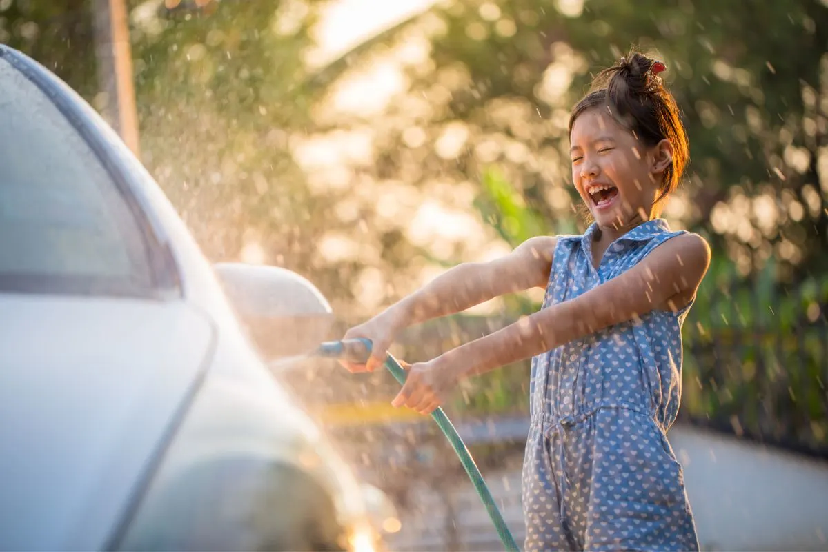 middle school girl with water hose having fun cleaning car