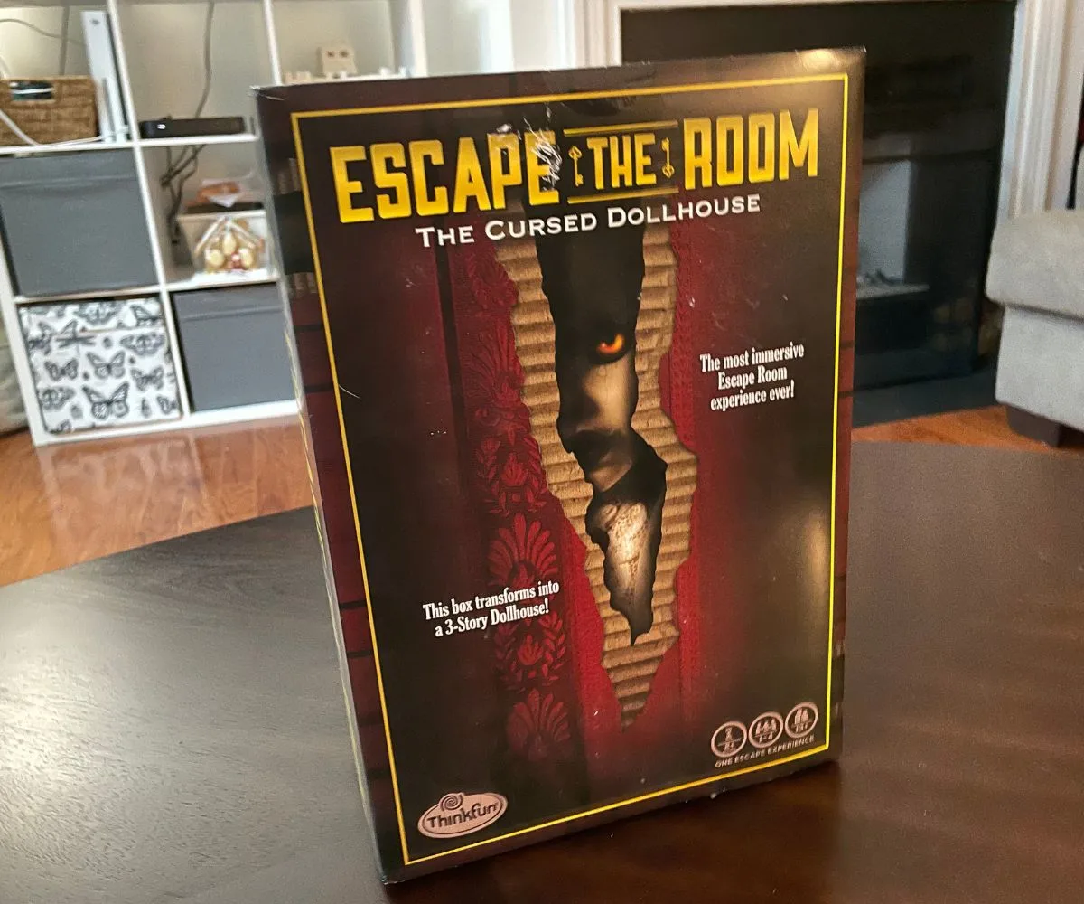 Escape the Room Dollhouse burgundy box with yellow writing on dark table