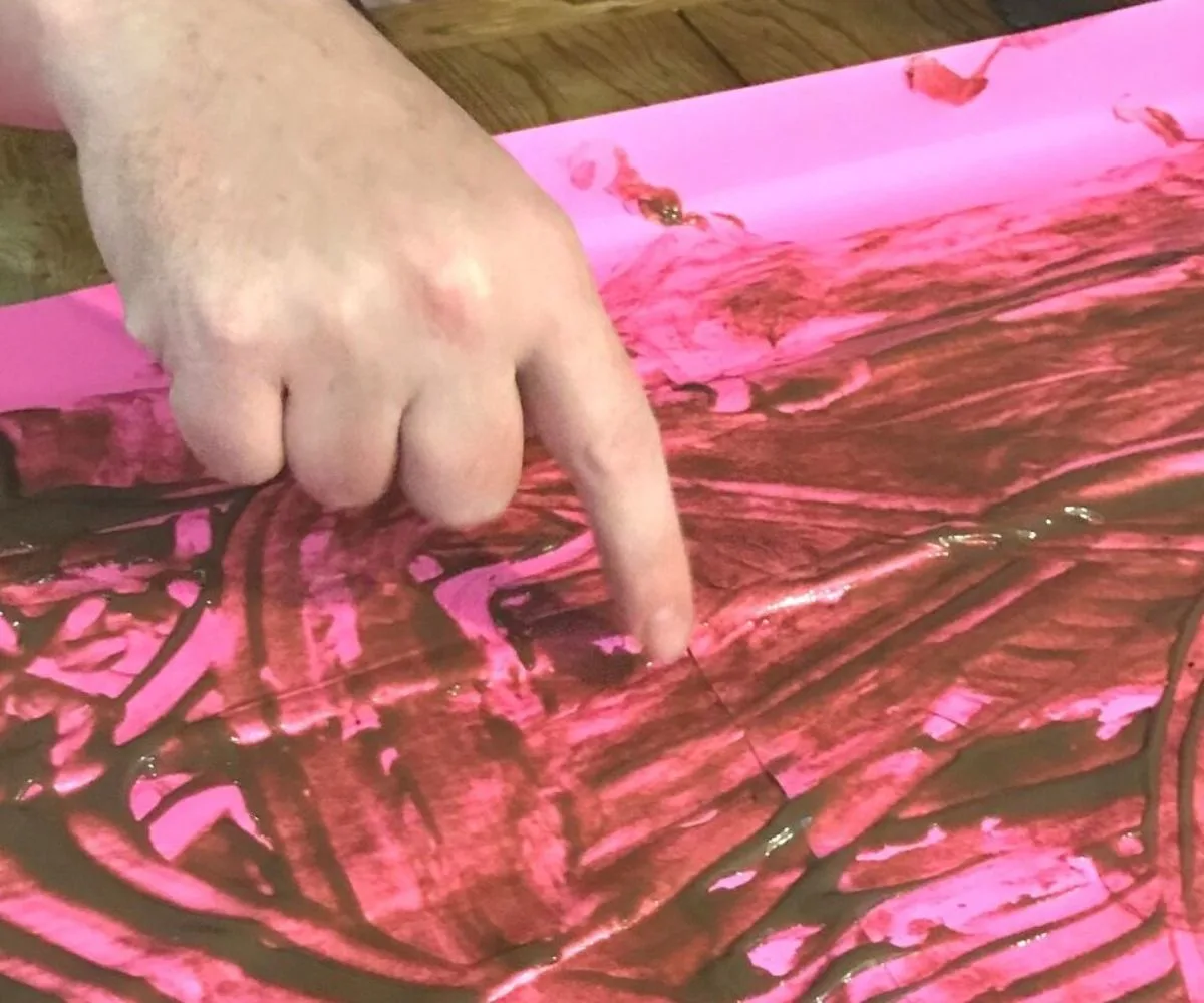 hand playing pudding pictionary on large hot-pink sheet of paper
