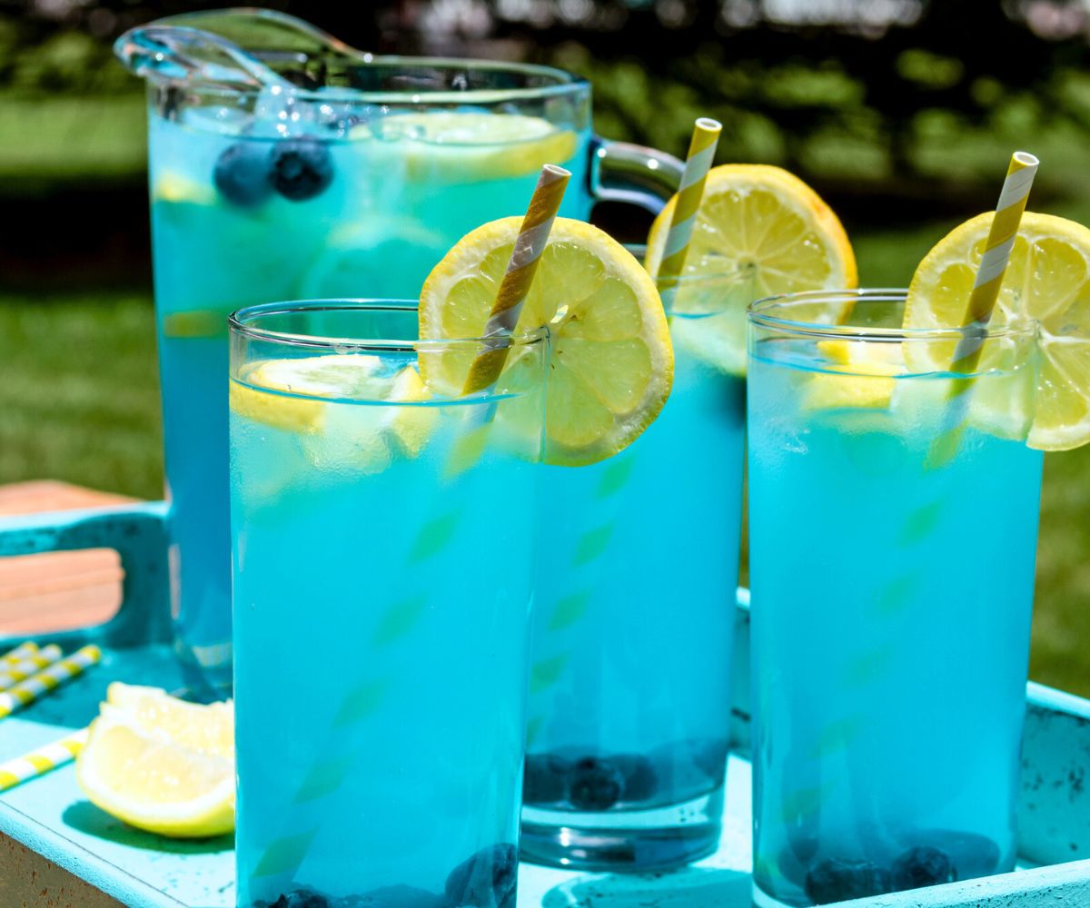 bright blue pitcher of blueberry lemonade on blue tray with glasses