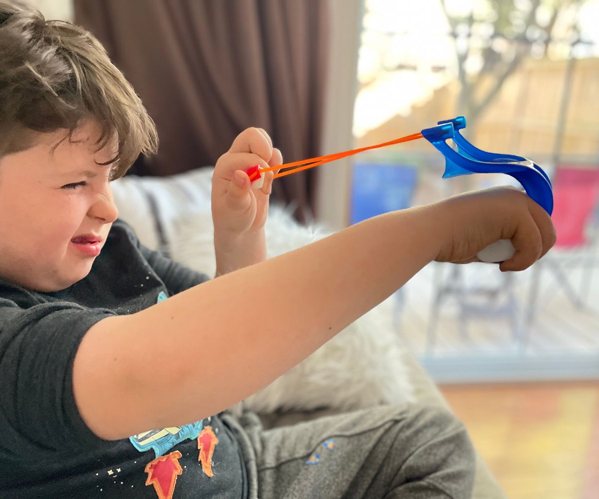 tween boy aiming marshmallow slingshot with one eye closed