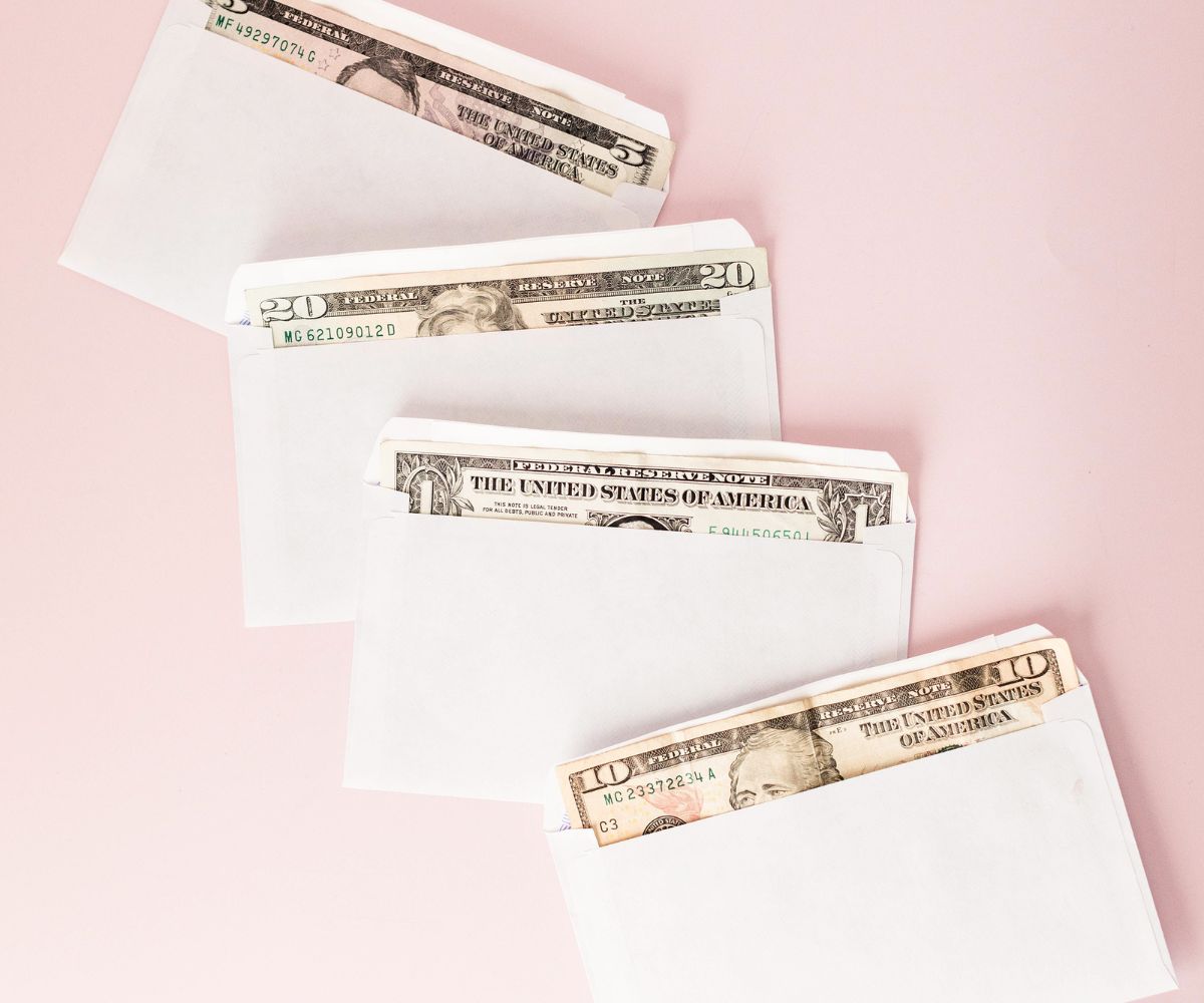 four white envelopes with money in each on a pink background