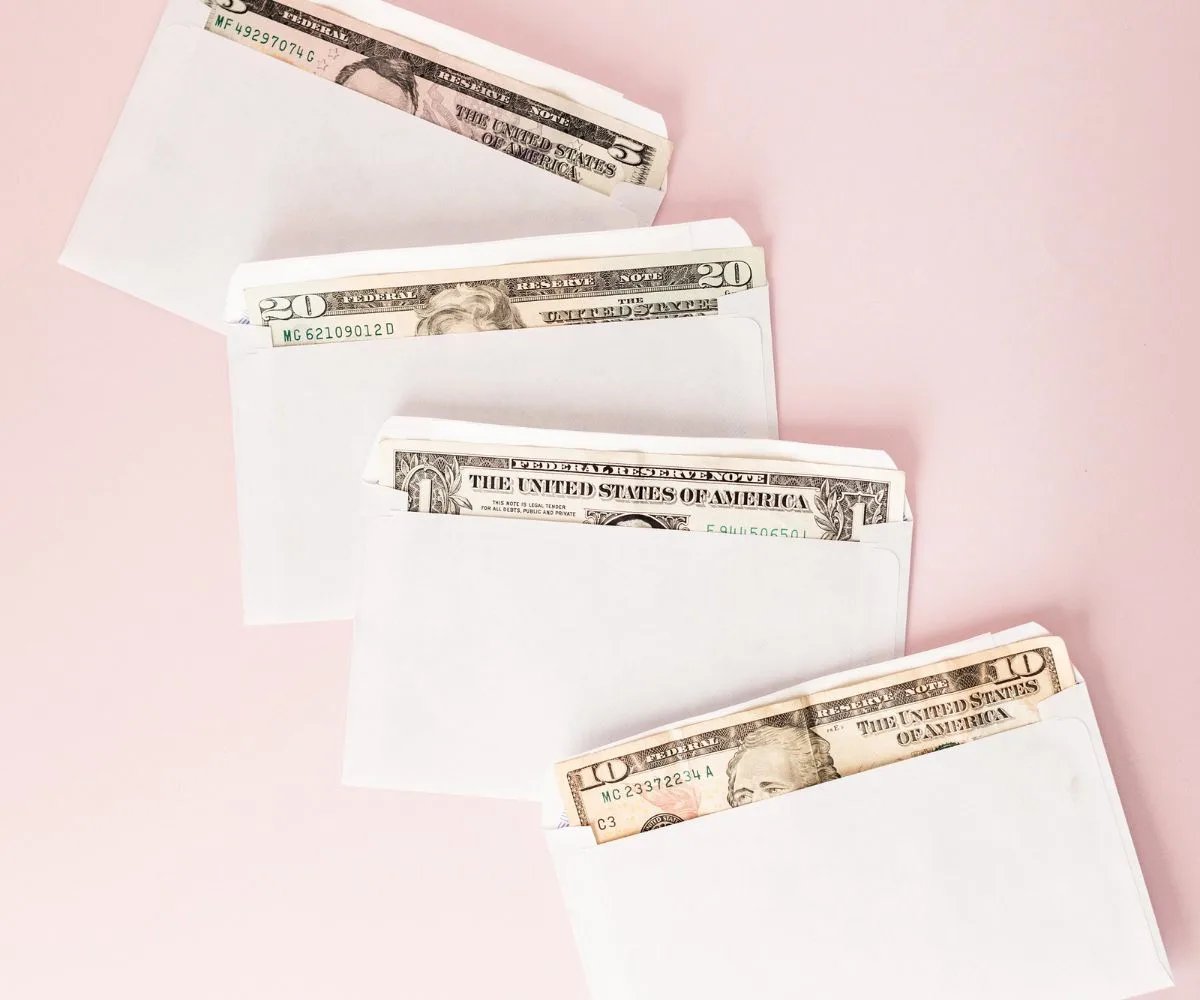 four white envelopes with money in each on a pink background