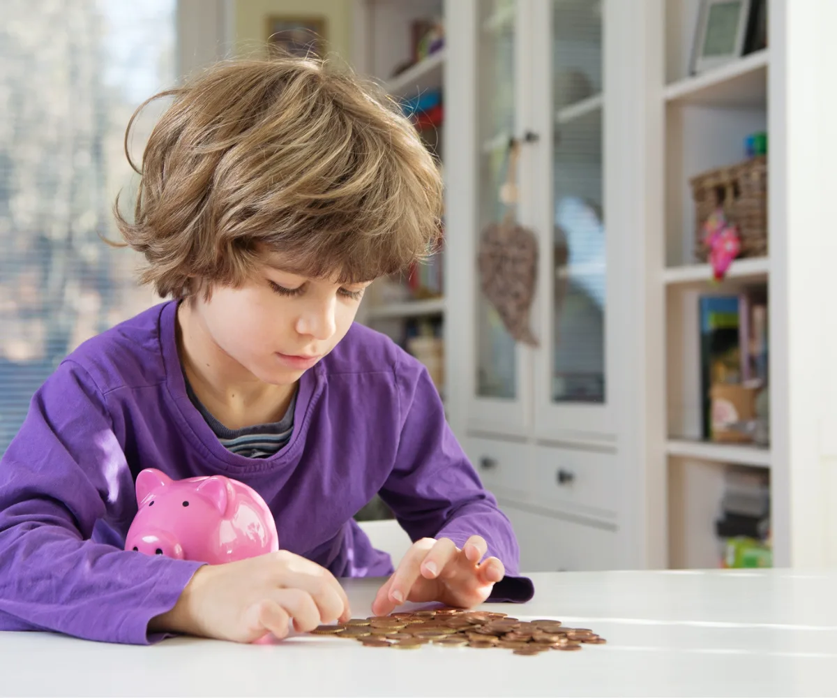 boy in purple shirt counting lots of pennies with piggy bank