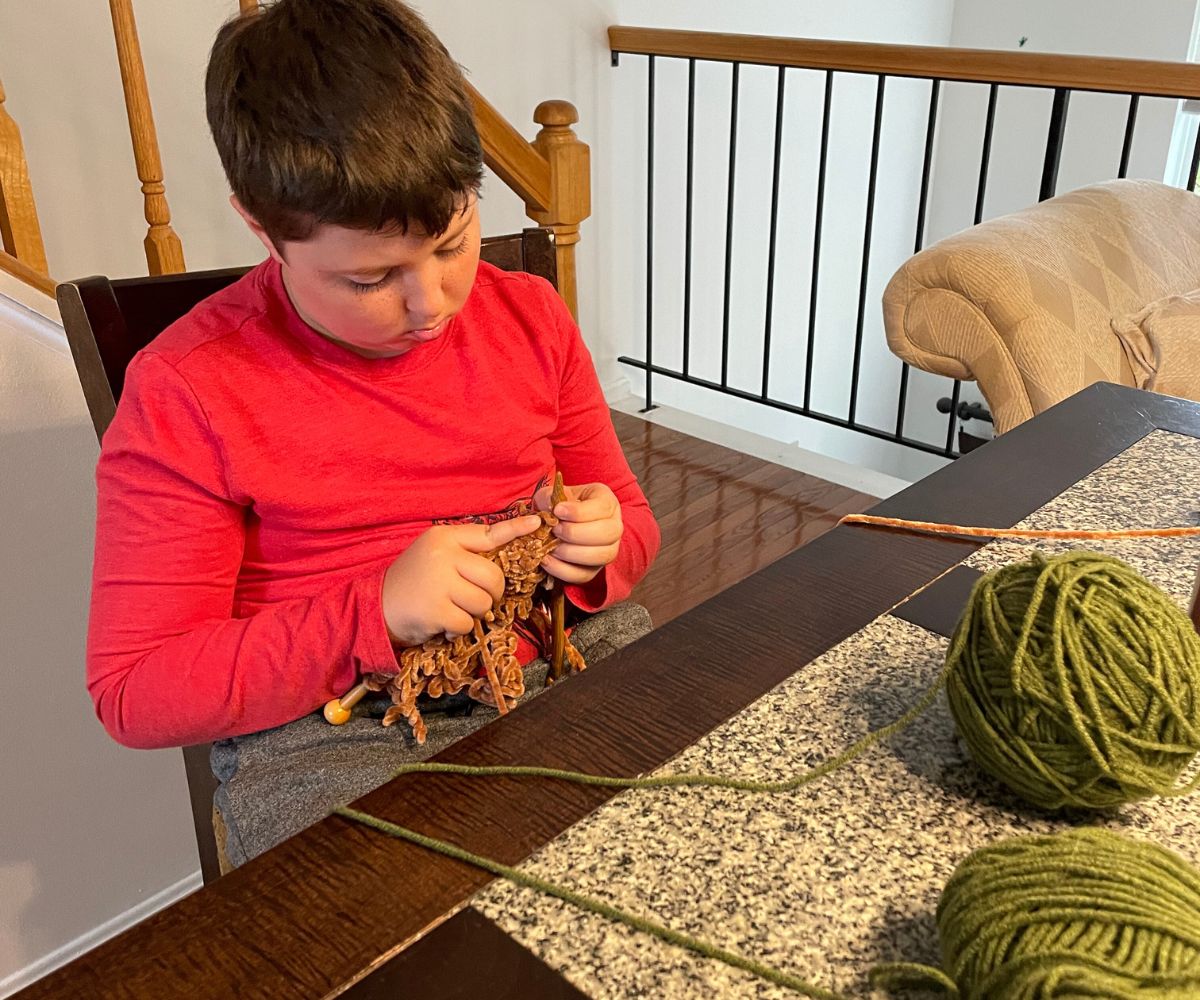 tween boy knitting at dining room table