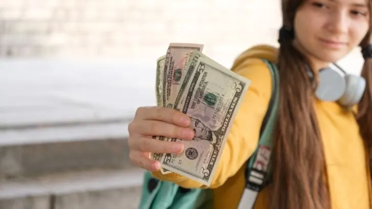 preteen girl in yellow sweatshirt holding money