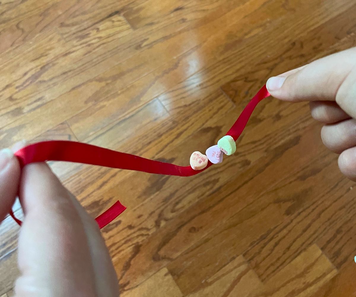 two people each holding one side of ribbon, and three candy conversation hearts in middle