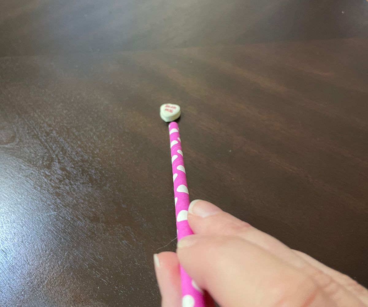 hand holder straw blowing towards a candy heart
