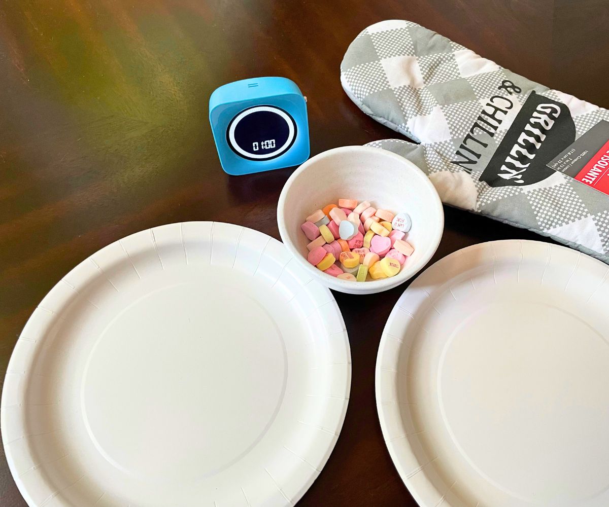 oven mitt that goes over hand, bowl of candy conversation hearts, two empty plates, and a blue timer set to 1 minute