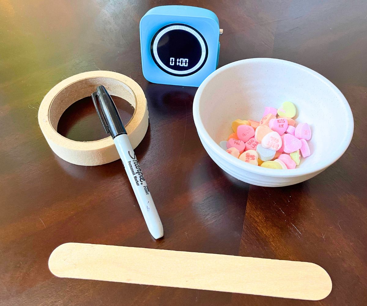 large popsicle stick, sharpie marker, masking tape, blue timer, and little bowl of conversation candy hearts