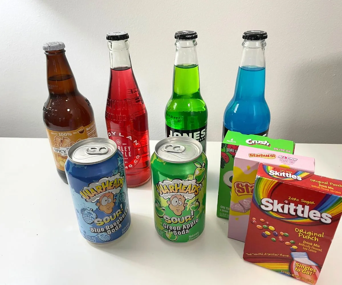 brightly colored glass sodas and Warhead cans of soda with drink mix boxes