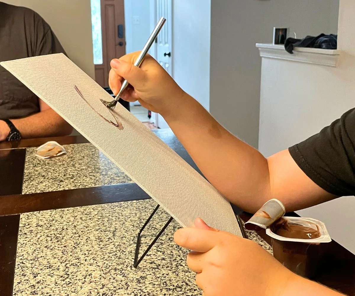 tween using paintbrush on canvas with pudding cup to dip in