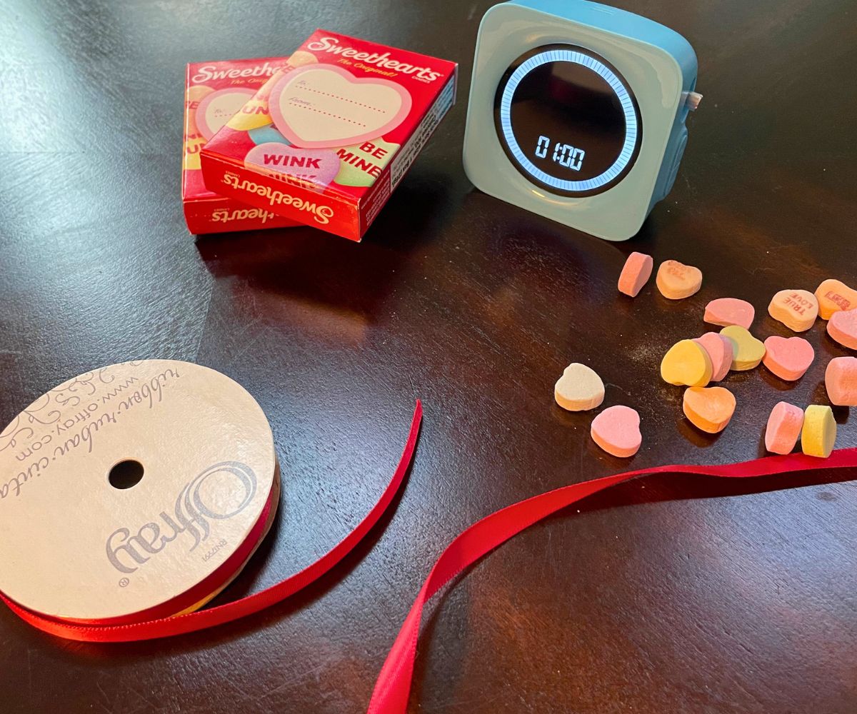 thin red ribbon spool, candy conversation hearts boxes, and blue timer on dark table
