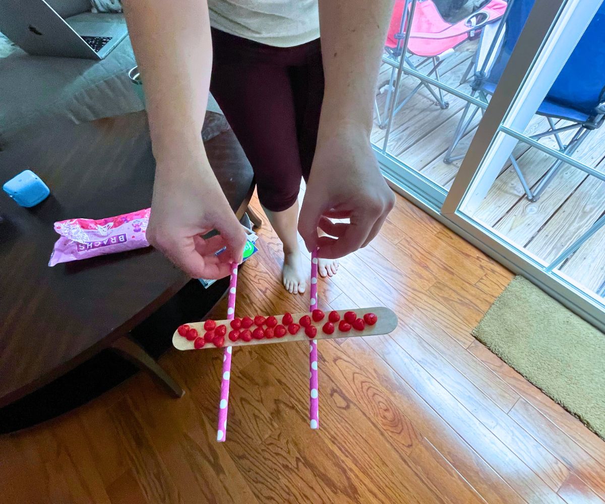woman holding two straws, transporting the red cinnamon hearts candies on the popsicle stick