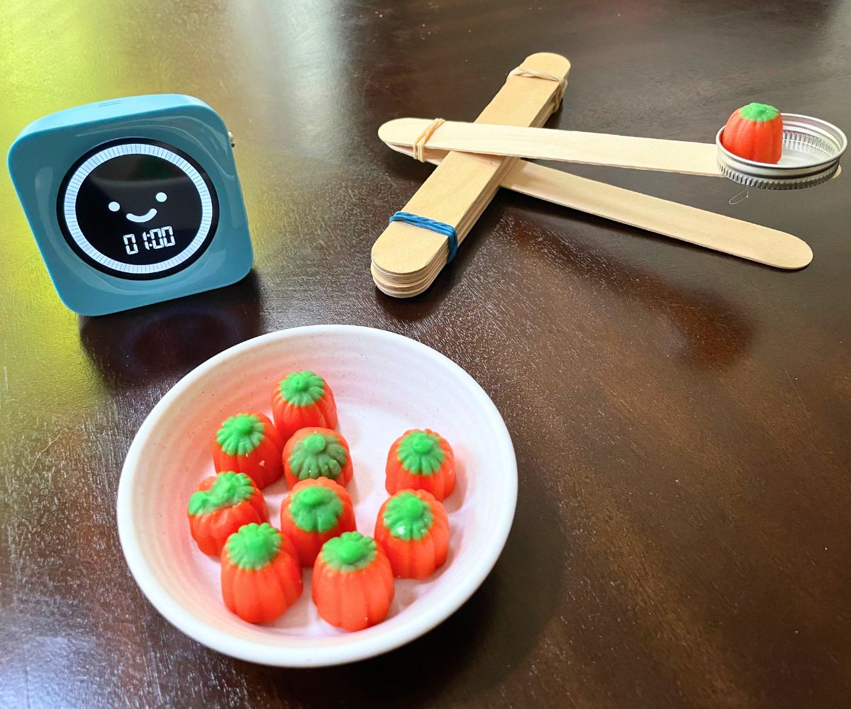 pumpkin candy in homemade catapult, next to blue timer marked at 1:00