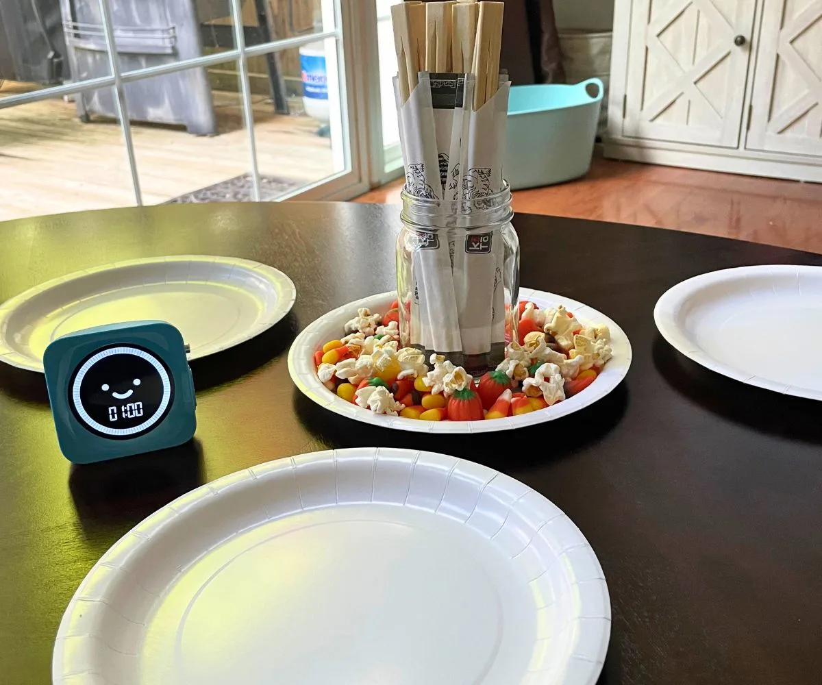 three white paper plates around a plate filled with candy corn, pumpkins, and popcorn, and a mason jar filled with chopsticks