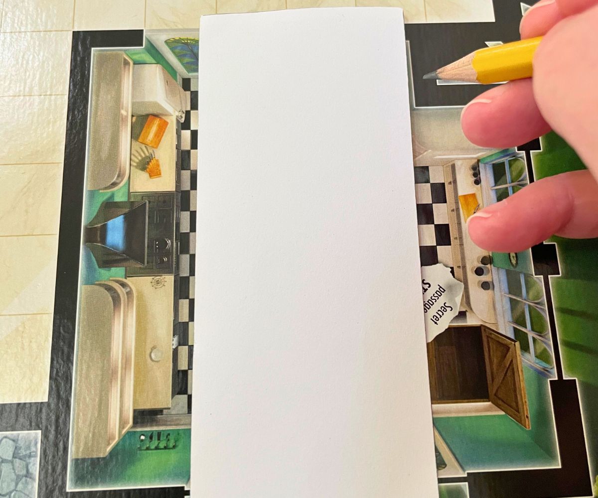 part of Clue board with white bookmark template and person with pencil tracing it