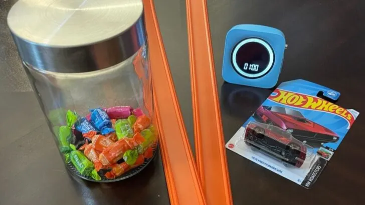 mini car, two car tracks, jar of wrapped candy, and one minute timer on dark table