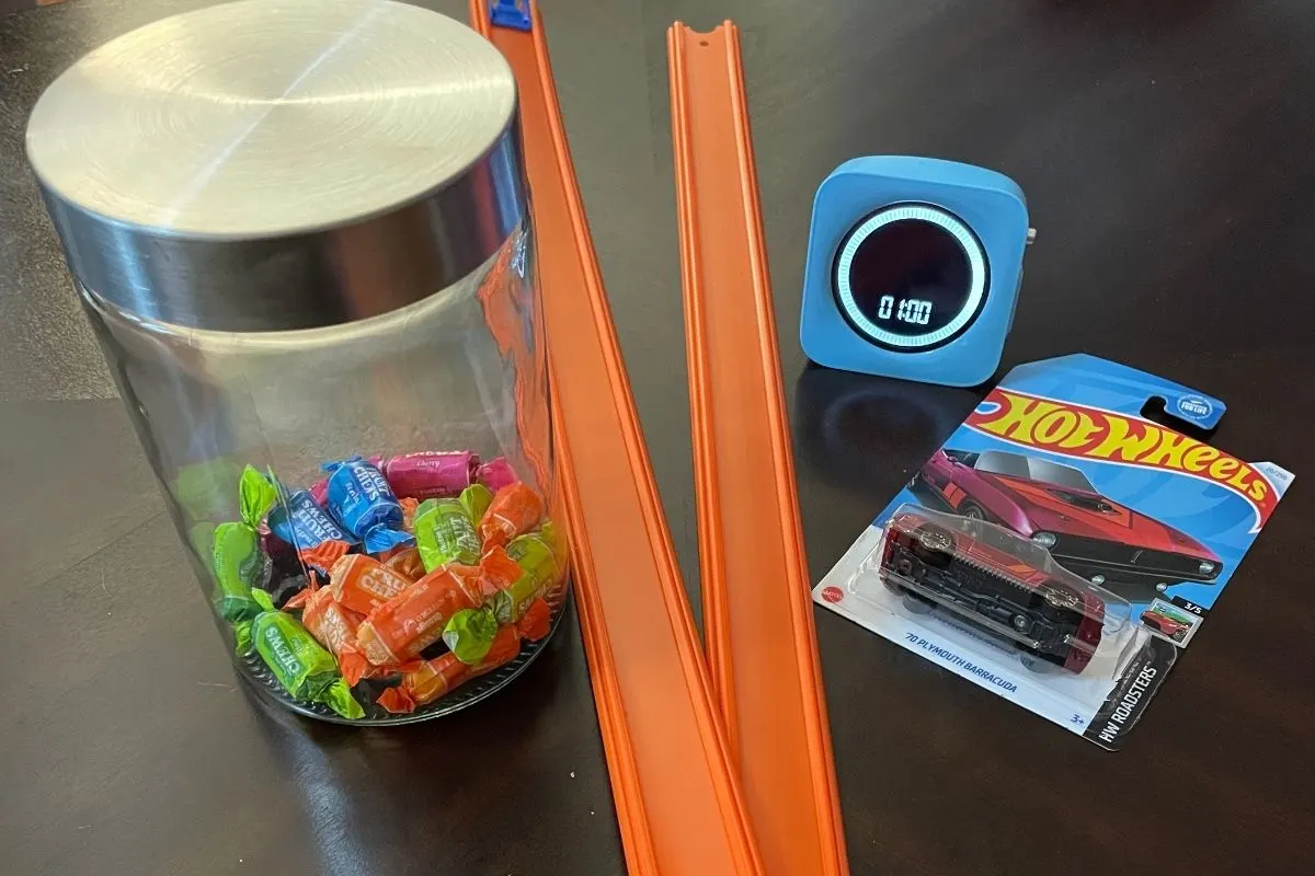 mini car, two car tracks, jar of wrapped candy, and one minute timer on dark table