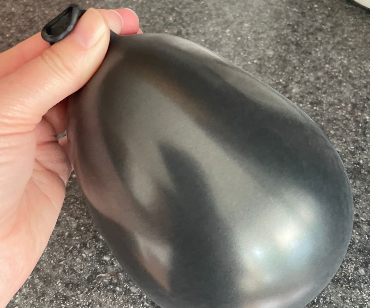 woman holding top of black blown up balloon