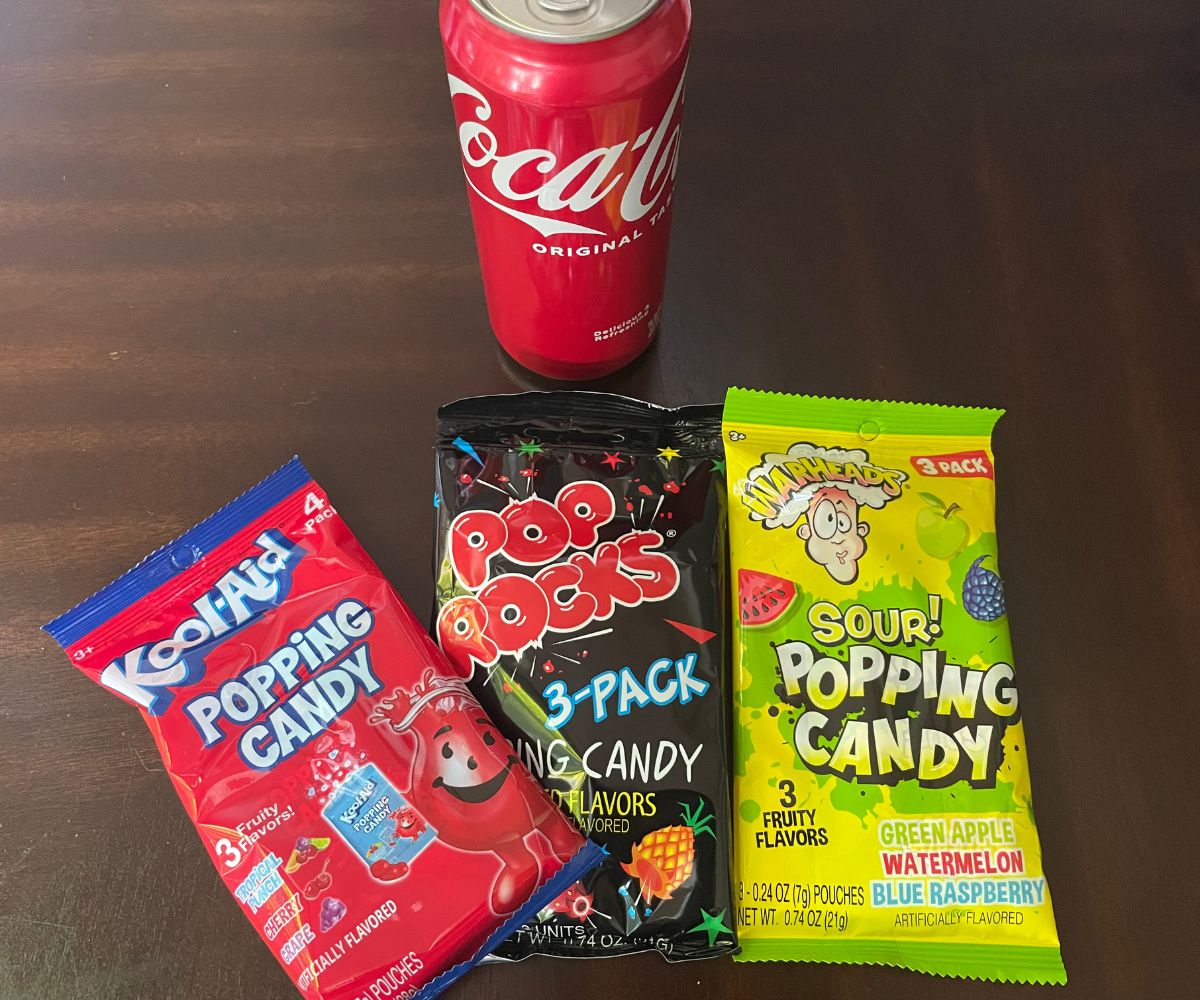 three bags of different brands' popping candy, and one Coca-Cola can on dark table