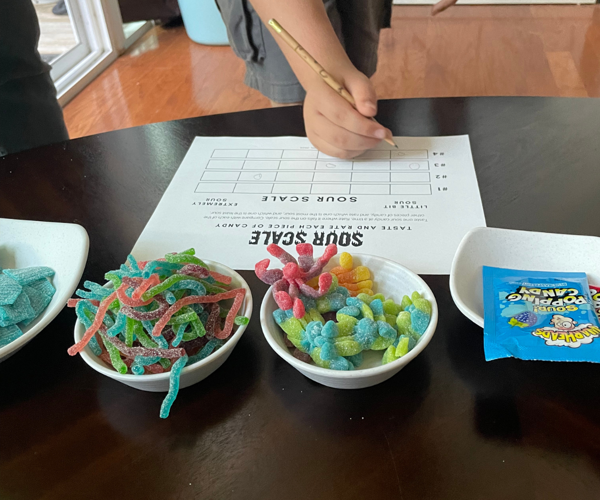four sour candies in bowls with preteen boy writing his score on the Sour Scale sheet