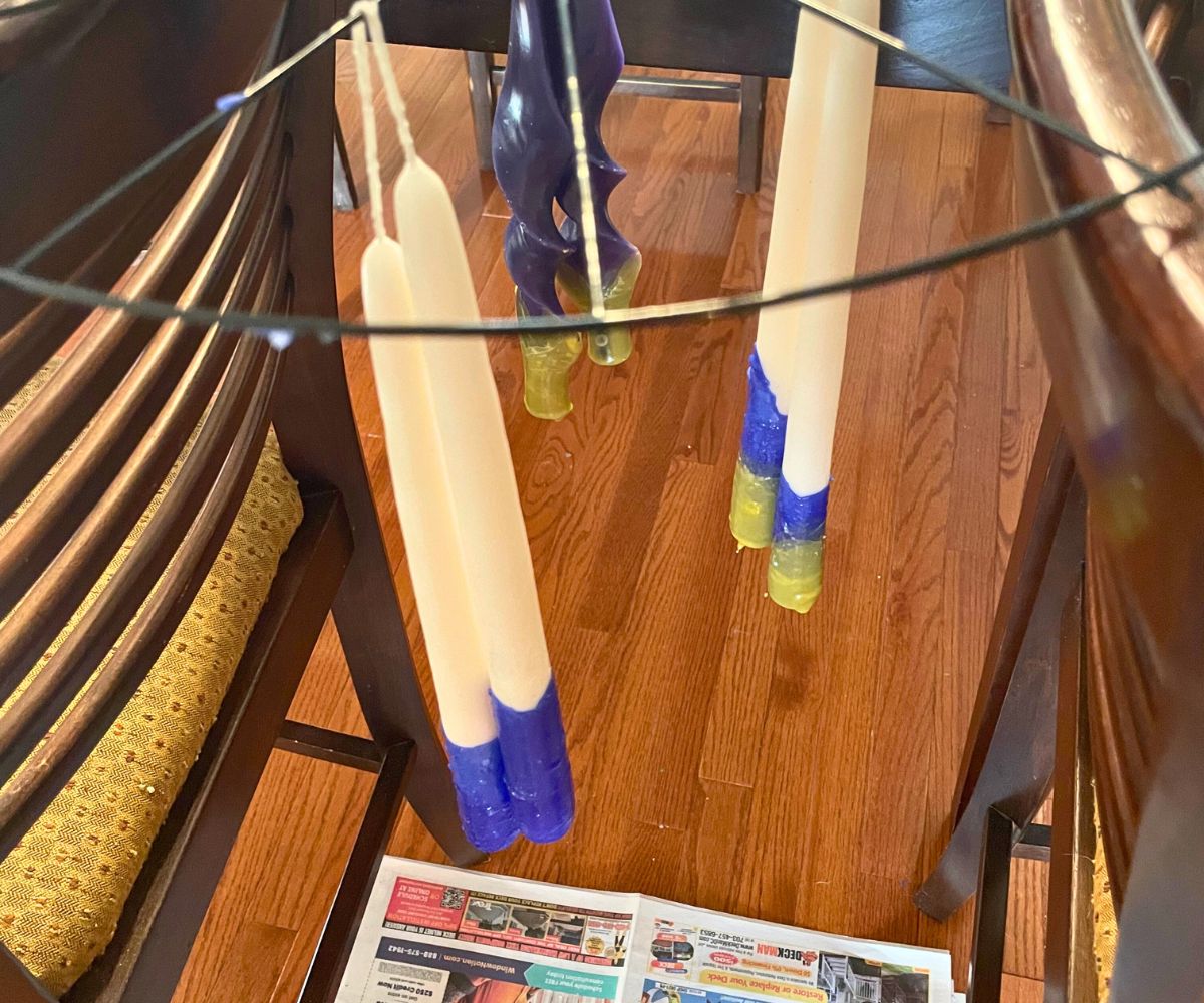 long taper candles dipped in blue wax drying on wire rack hanging between two chairs