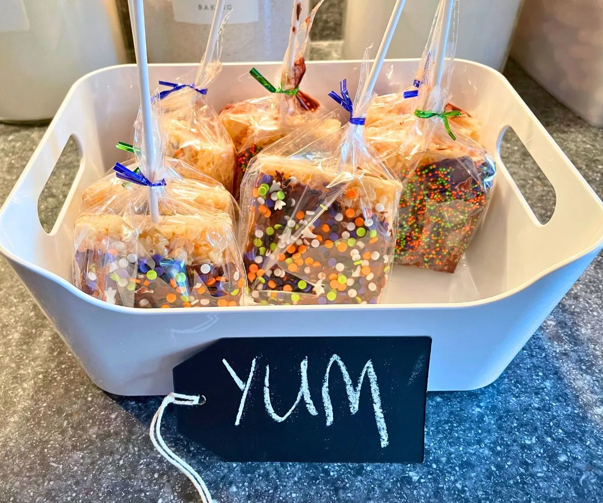 7 rice krispies treats pops upside down sitting in white bin with chalkboard tag "yum"