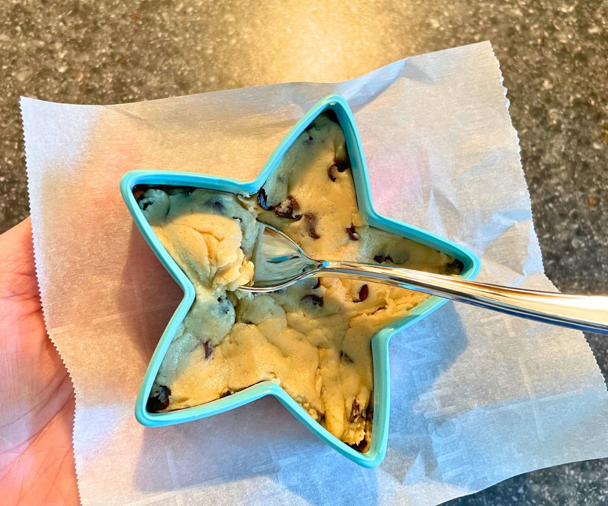light teal blue lined star cookie cutter filled with edible cookie dough, woman holding it to eat