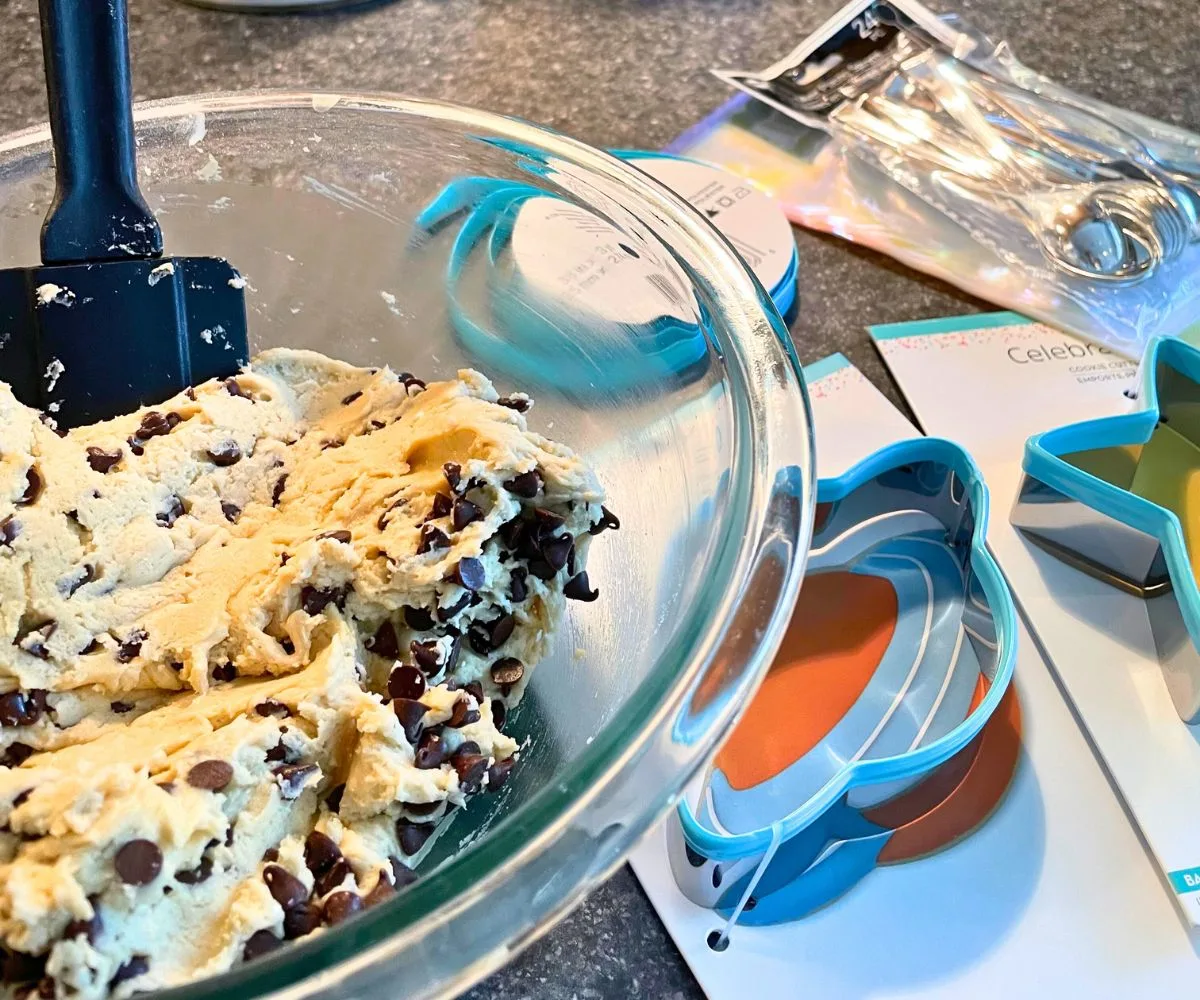 bowl of edible cookie dough, next to two cookie dough cutters, silver spoons, and ribbon