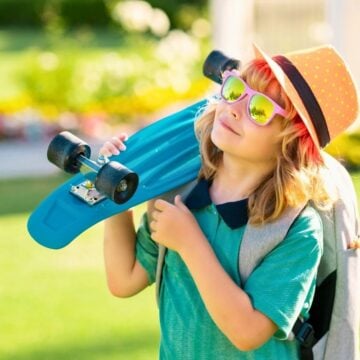 boy in brightly colored clothes smiling looking up at sky, holding skateboard