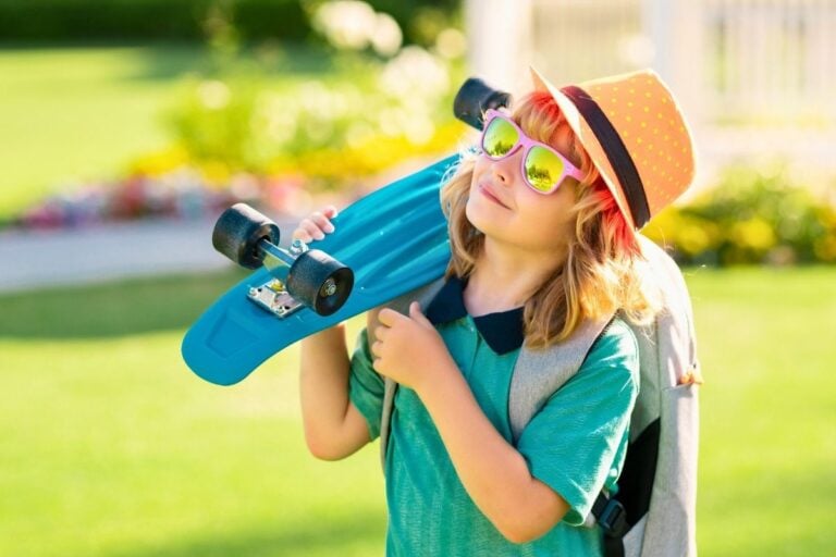 boy in brightly colored clothes smiling looking up at sky, holding skateboard