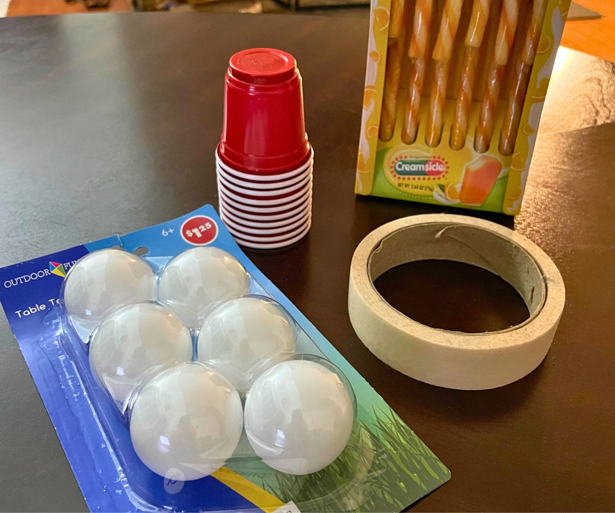 candy canes, small red cups, masking tape, and ping pong balls on dark table