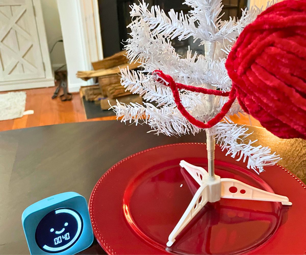assembled white tree standing on red plate, with person putting yarn strings around it and timer at 40 seconds left