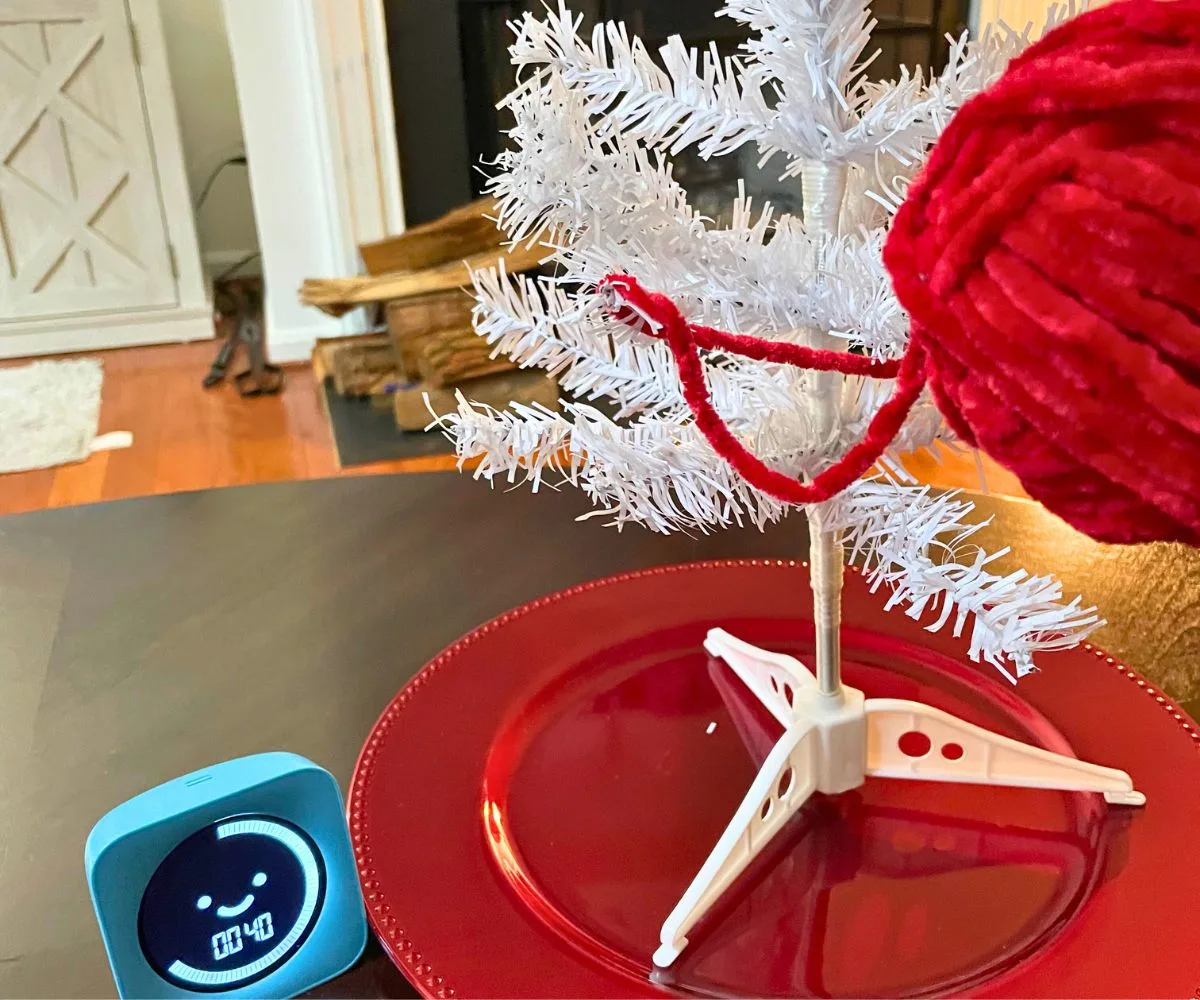 assembled white tree standing on red plate, with person putting yarn strings around it and timer at 40 seconds left