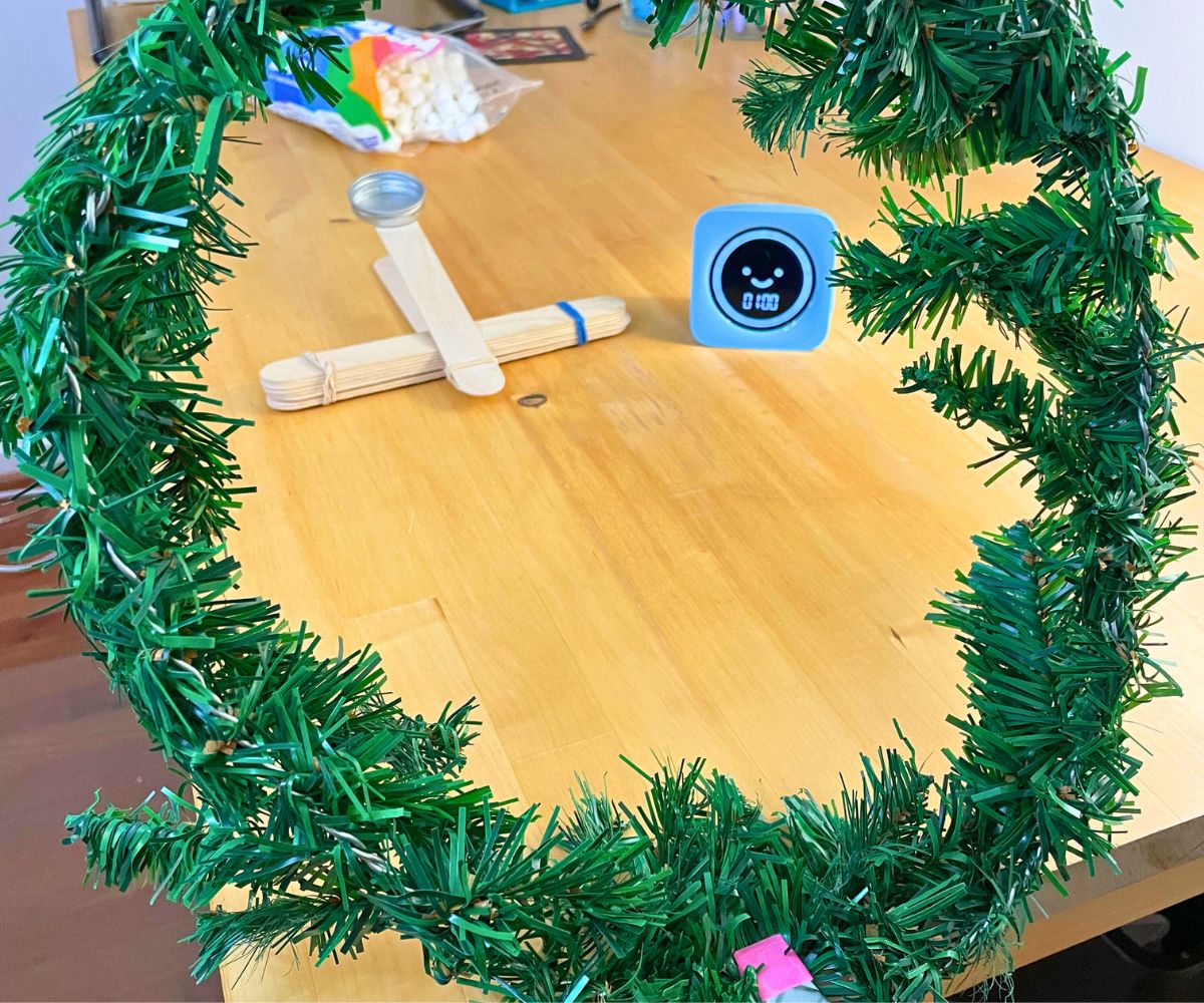 wreath standing upright clamped to table, showing catapult, timer, and marshmallows