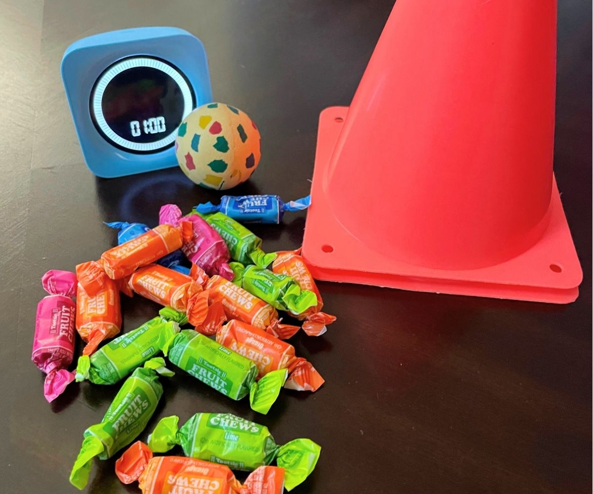 two bright orange safety cones, 1 minute timer, bigger rubber ball, and pile of wrapped candy