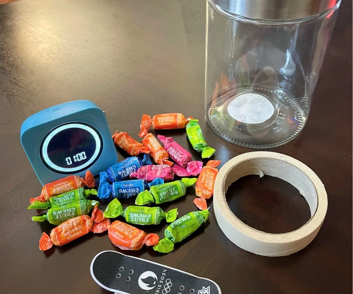 mini skateboard, masking tape, jar, wrapped candies, and 1 minute timer
