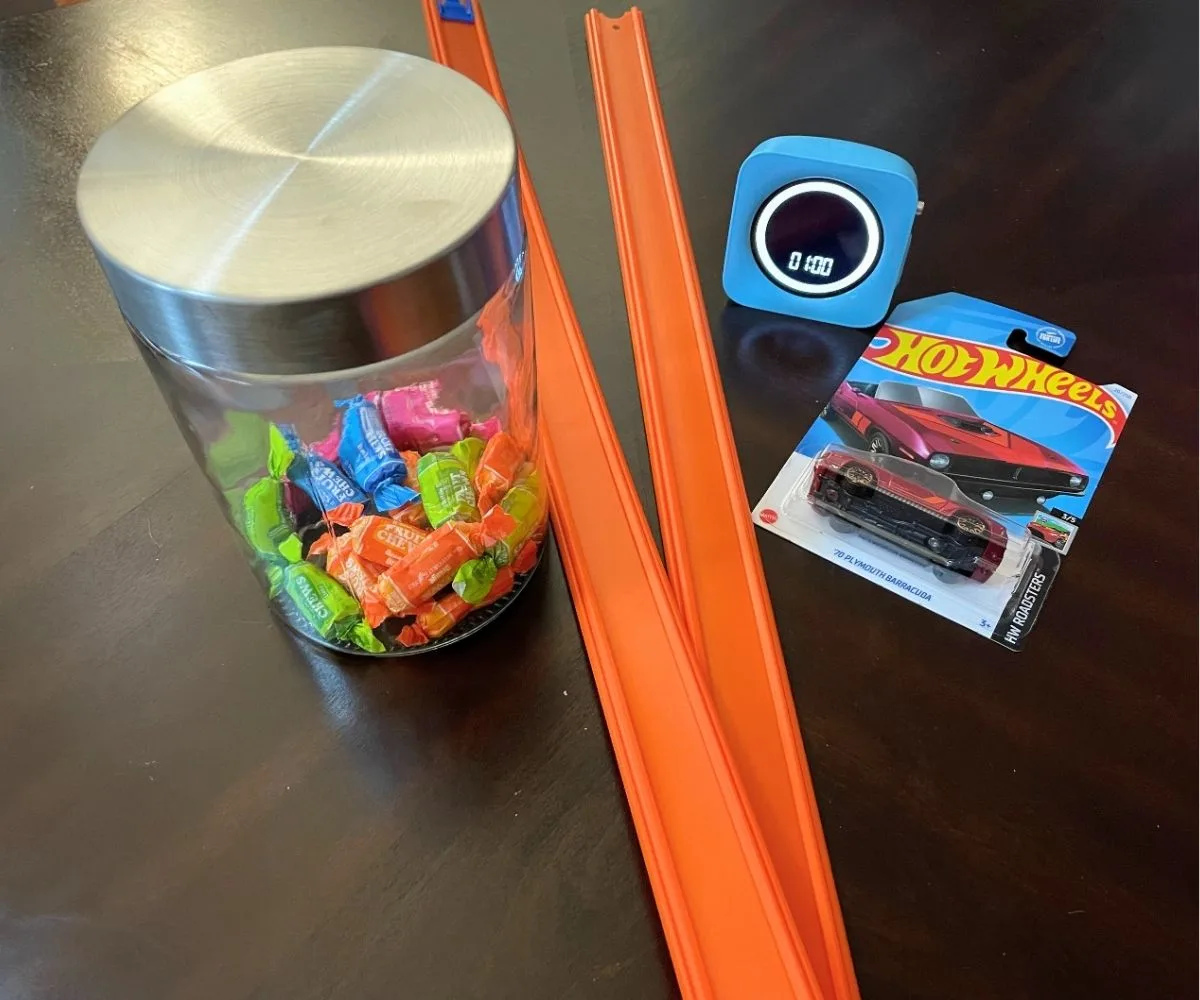 two car tracks, mini hot wheels, jar of candy, and 1 minute timer on dark table