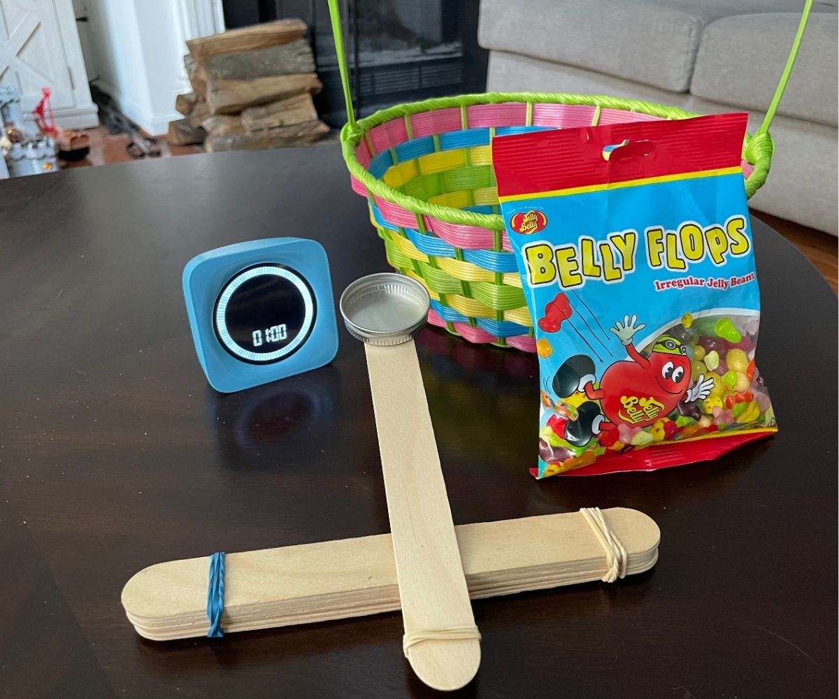 Jelly Belly Flops beans, timer set at 1 minute, homemade catapult, and Easter basket on dark table