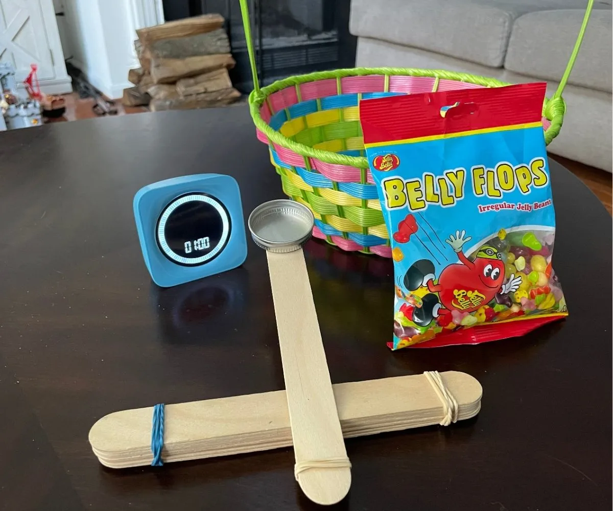 Jelly Belly Flops beans, timer set at 1 minute, homemade catapult, and Easter basket on dark table