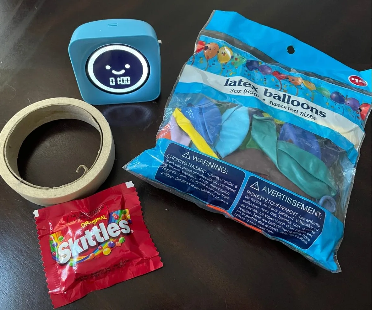package of balloons, masking tape, skittles, and a timer set for 1 minute