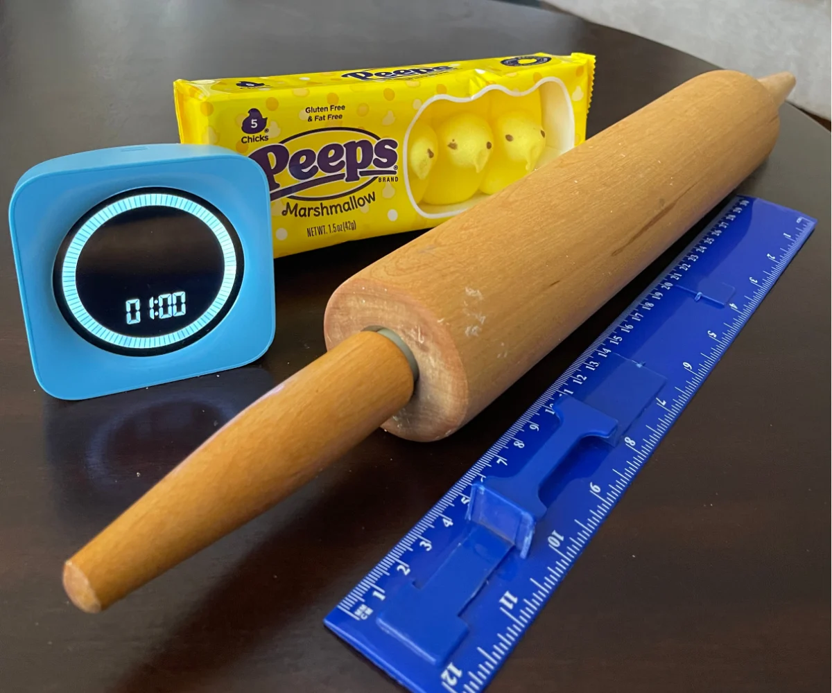 rolling pin, ruler, bag of yellow peeps, and timer set at one minute on dark table