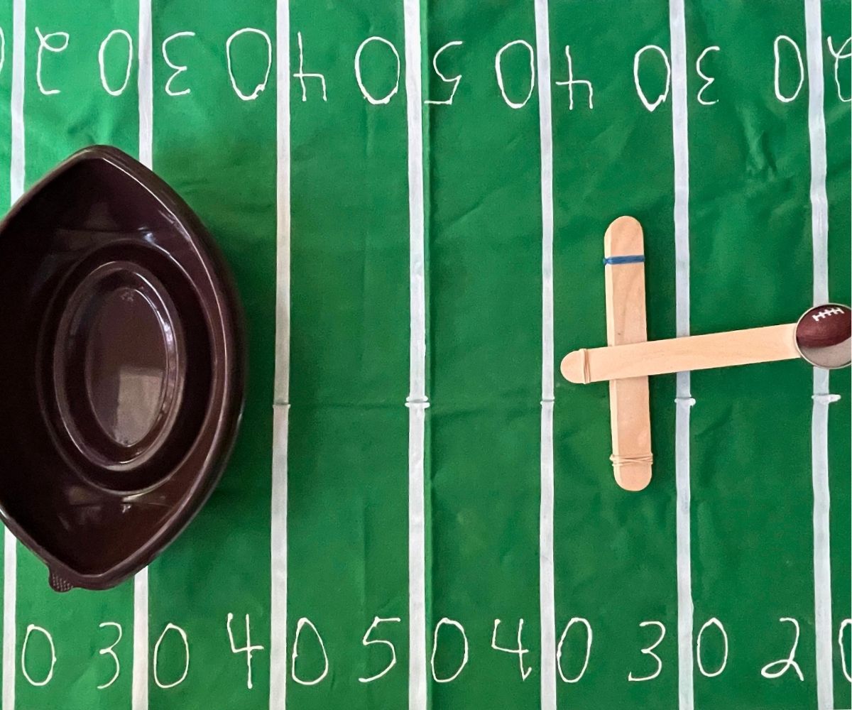 homemade catapult holding toy football with empty football snack container on other side, on football field tablecloth