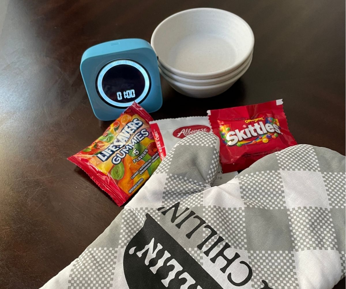 big kitchen oven mitt with little packages of skittles, gummies, and lifesavers gummies, timer set to 1 minute and little containers